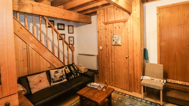 Ett mysigt rum med en trätrappa, en svart soffa med mönstrade kuddar, ett träbord och en stol.