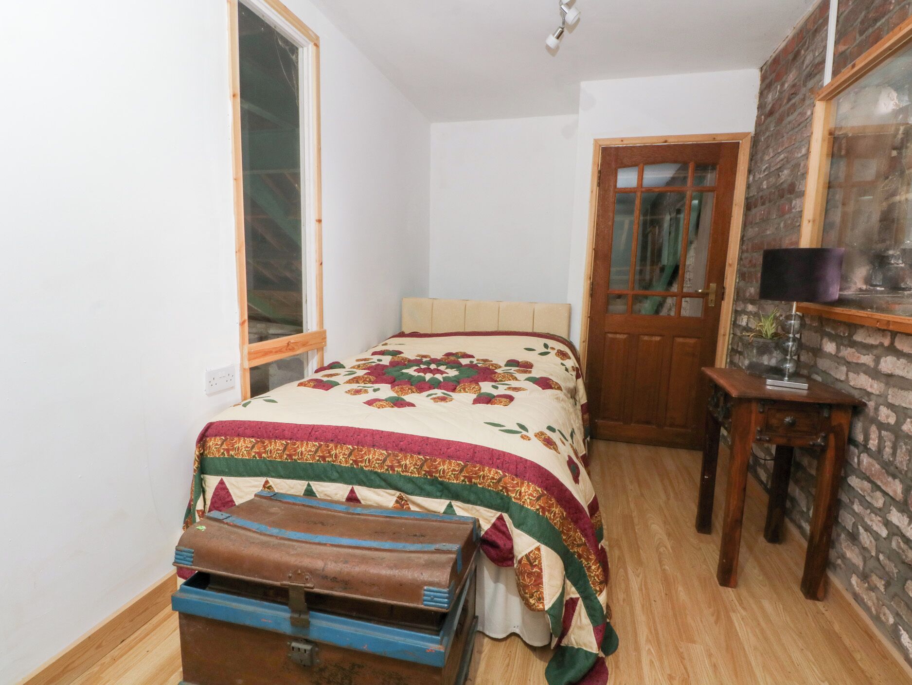 Un dormitorio con una cama, una mesita de noche de madera, una ventana y una puerta.