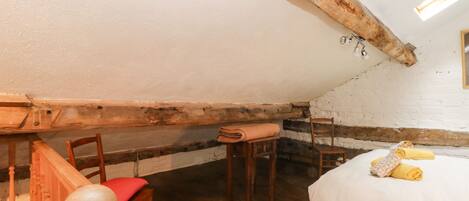 Quarto de sótão acolhedor com vigas de madeira expostas, uma cadeira de madeira, uma pequena mesa de madeira e uma cama com toalhas dobradas com cuidado.