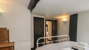 A bedroom with a bed, a bedside table, a lamp, and a door leading to another room. - Woodloft Cottage (Ambleside)