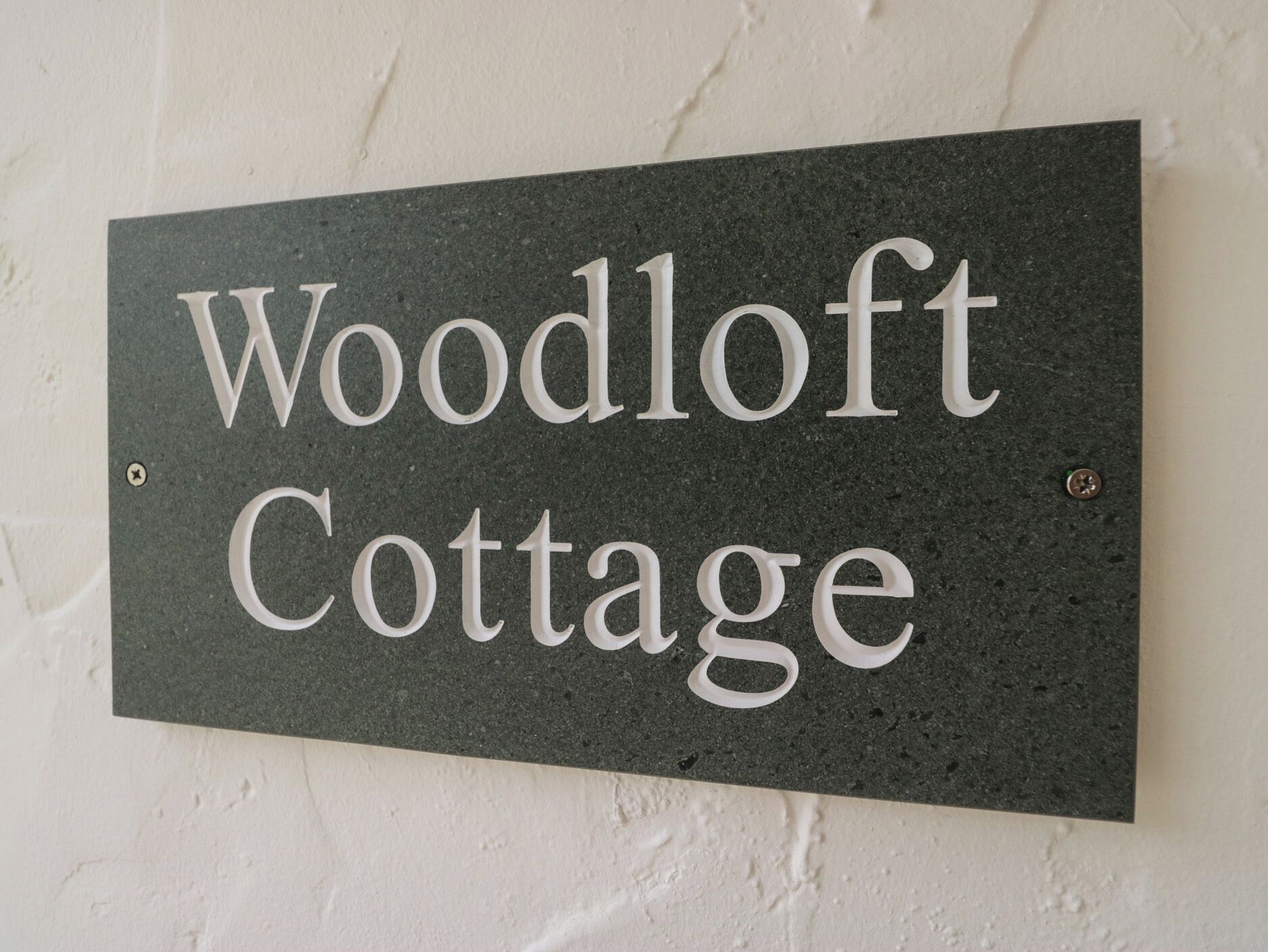 Une enseigne portant l’inscription « Woodloft Cottage » sur un fond sombre et texturé.