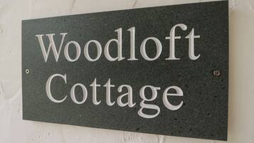 Une enseigne portant l’inscription « Woodloft Cottage » sur un fond sombre et texturé.