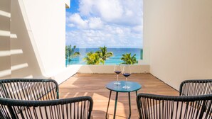 Ein Balkon mit Meerblick, zwei Weingläser auf einem kleinen Tisch und Korbstühle.