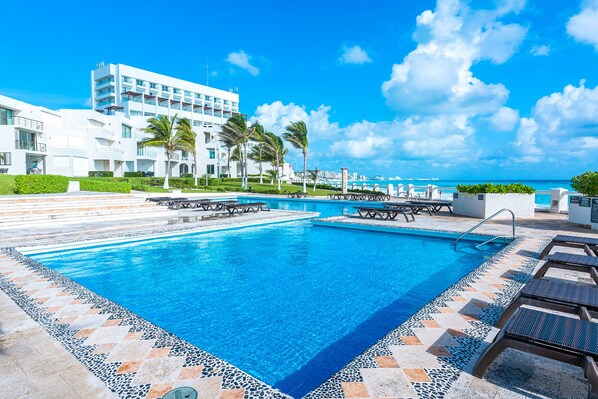 A swimming pool with lounge chairs and a view of the ocean.