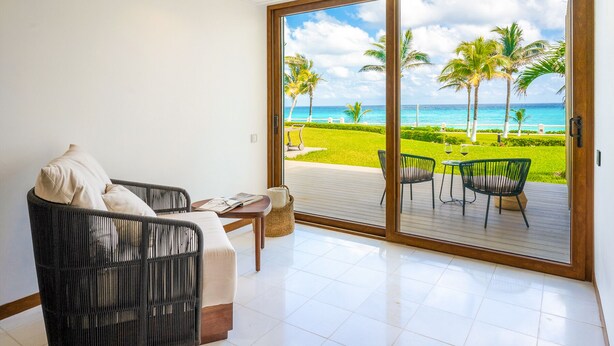 Ein Zimmer mit einer großen Schiebeglastür, die auf eine Terrasse mit Blick auf das Meer und Palmen führt.