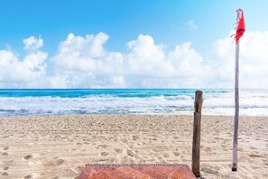 A sandy beach with a wooden post and a red flag, under a clear blue sky.