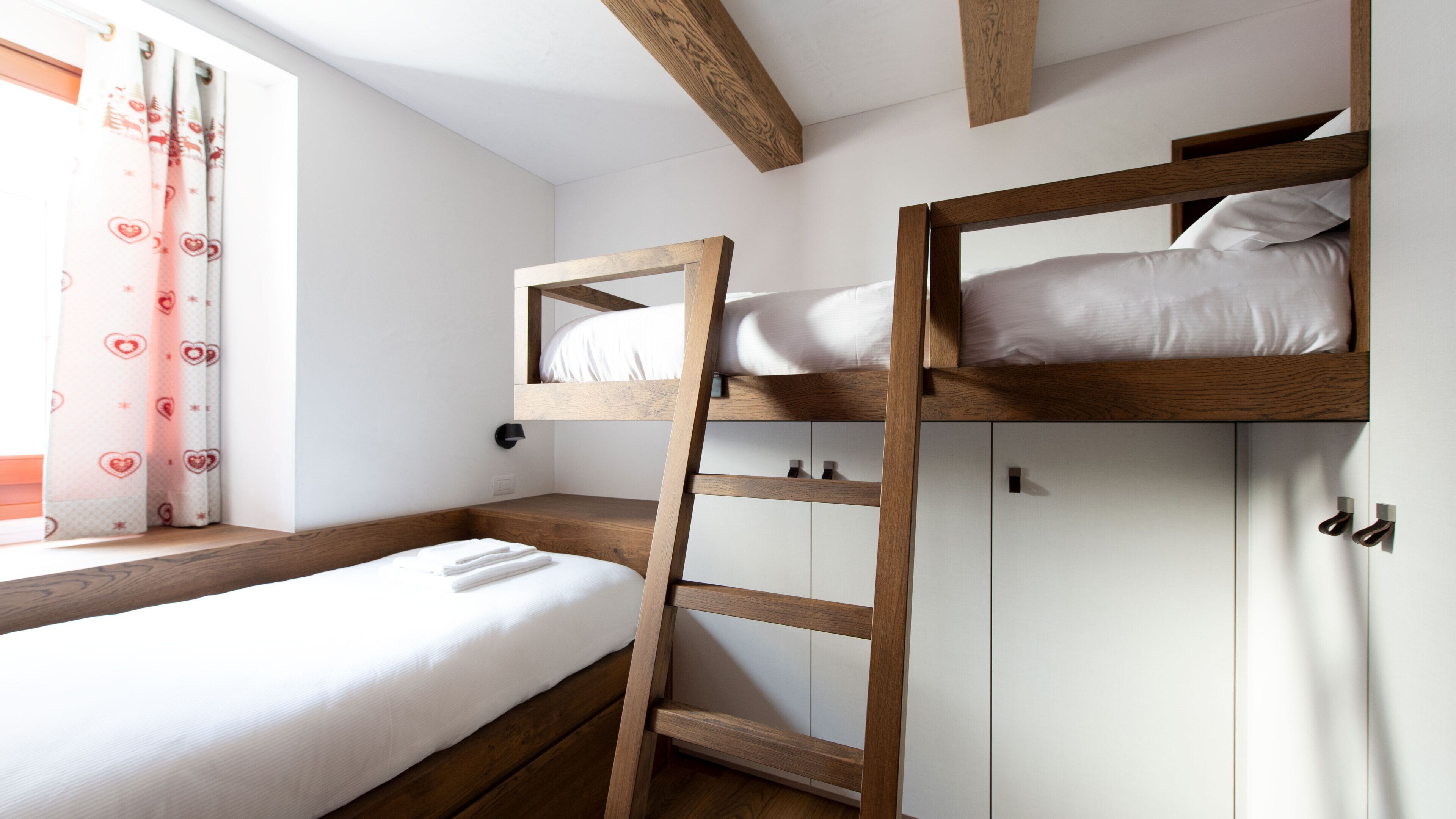 Une chambre avec un lit superposé, une échelle, une fenêtre avec des rideaux et une armoire blanche.