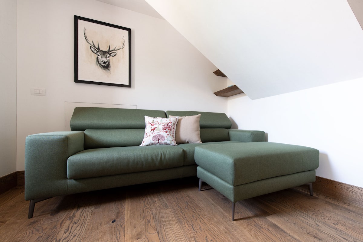 A modern living room with a green sectional sofa, a framed deer head artwork, and a sloped ceiling.