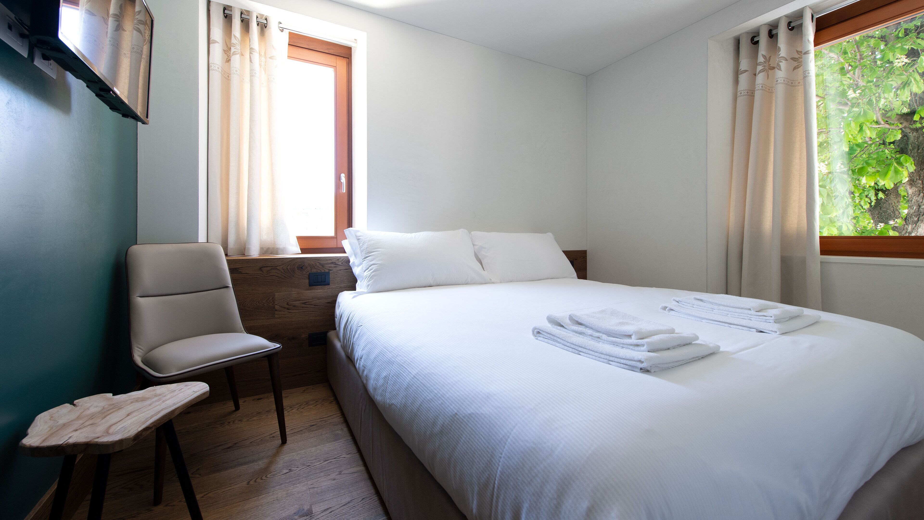 A hotel room with a bed, a chair, a wooden nightstand, and a window with curtains.