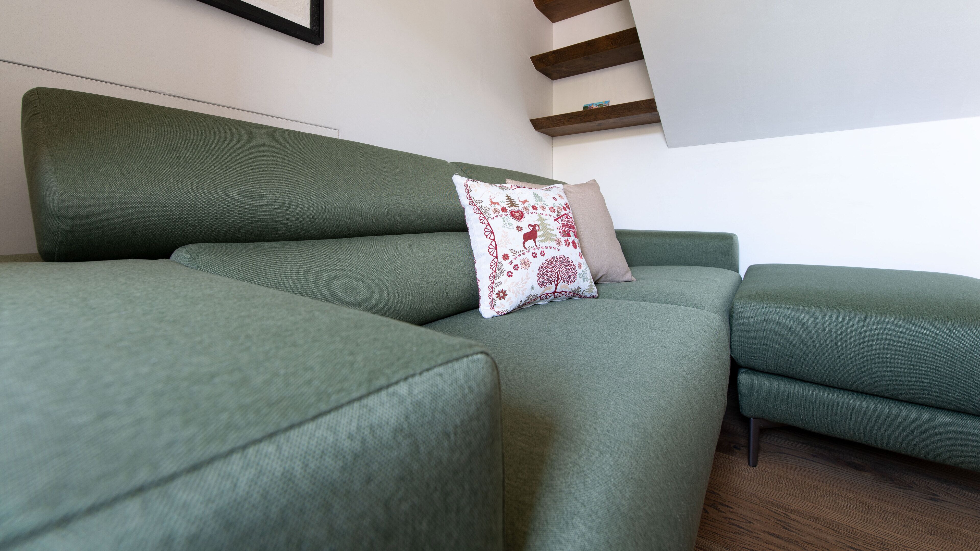 Un sofá verde con un cojín decorativo y suelo de madera.