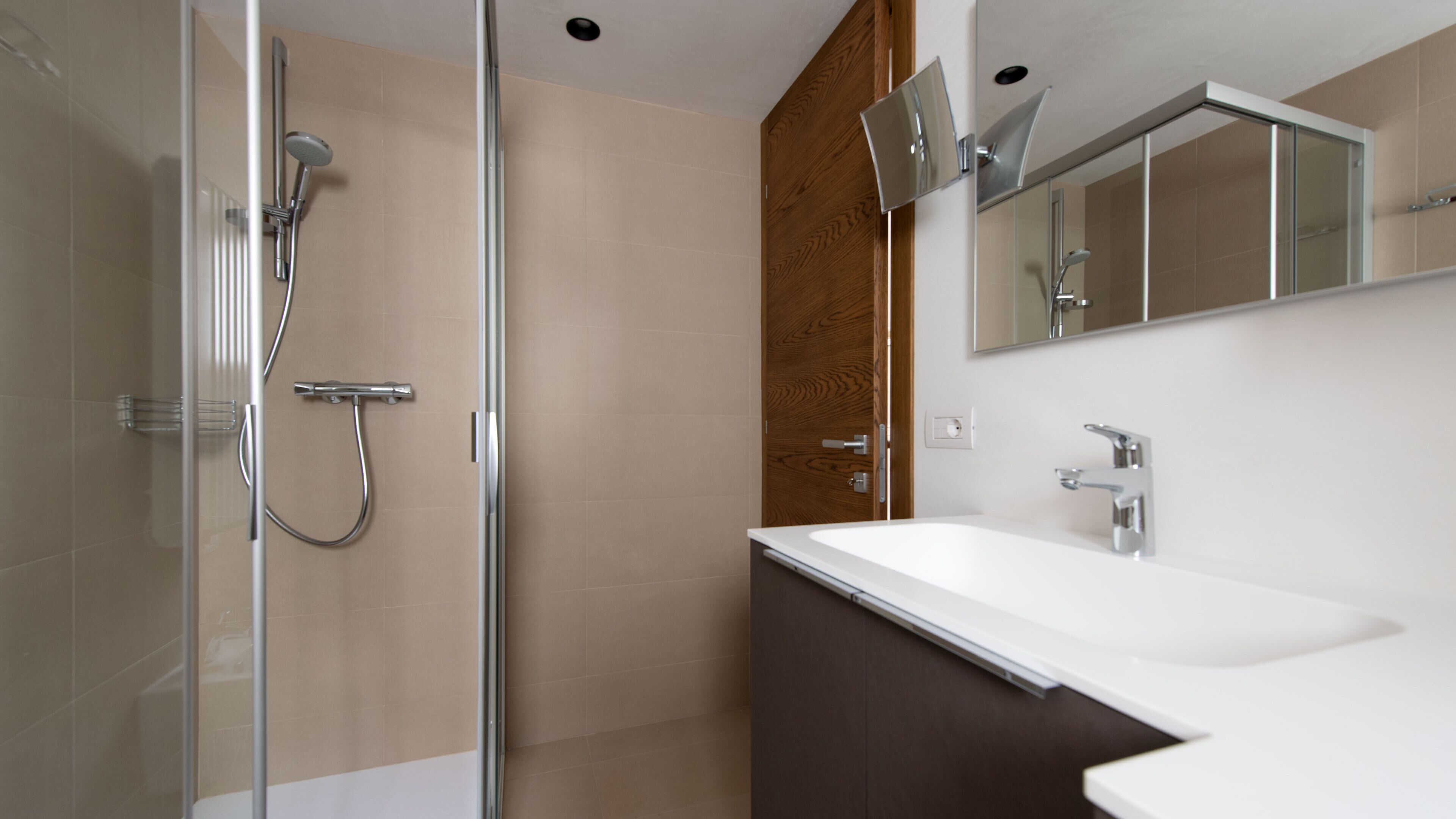 A modern bathroom with a glass shower enclosure, a wooden panel wall, and a white sink with a mirror above it.