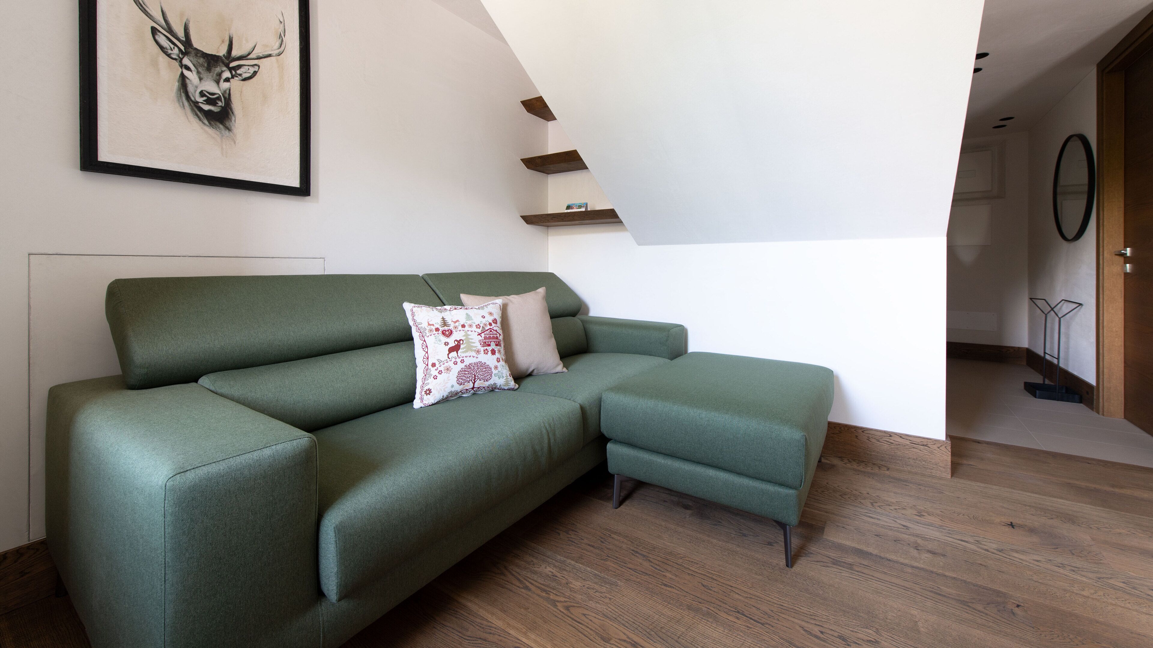 A green sectional sofa with a decorative pillow, a framed deer artwork on the wall, and a wooden floor.
