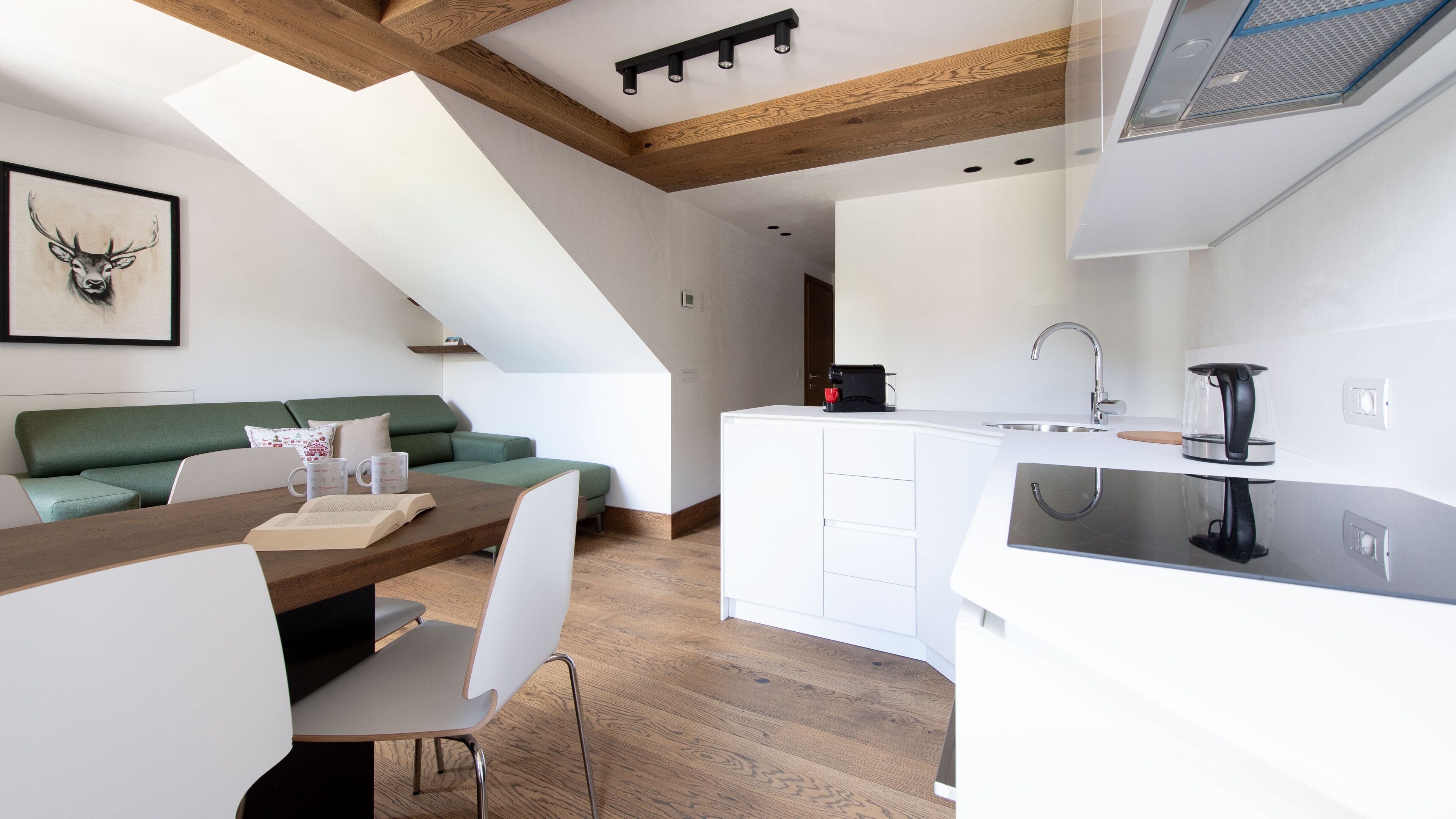 Eine moderne Küche mit weißen Schränken, einem Holzespeisetisch und einem grünen Sofa in einem Wohnbereich im Loft-Stil.