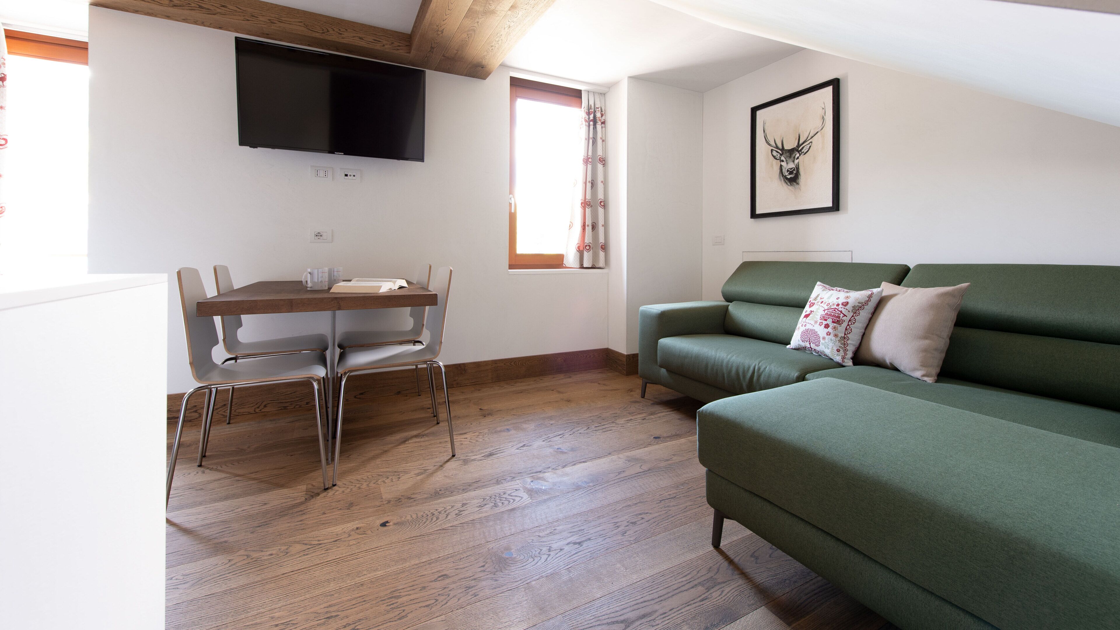 Ein modernes Wohnzimmer mit einem grünen Sofa, einem Holzesstisch mit Stühlen, einem flachbildfernseher an der Wand und einem gerahmten Kunstwerk mit einem Hirschkopf.