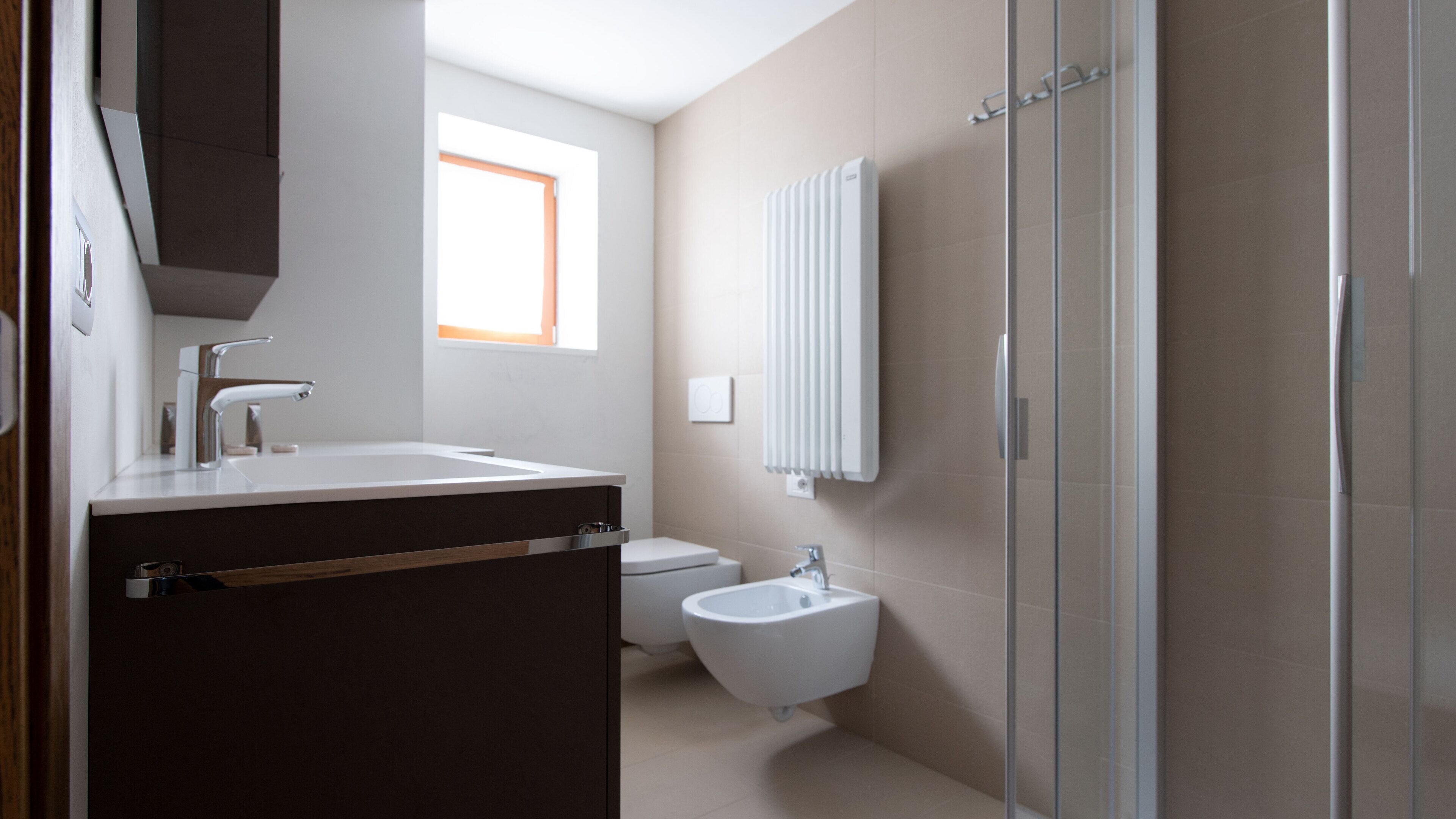 Ein modernes Badezimmer mit einem großen Waschbecken, einer Toilette und einem Bidet. Ein Fenster sorgt für natürliches Licht, und an der Wand befindet sich ein Spiegel.