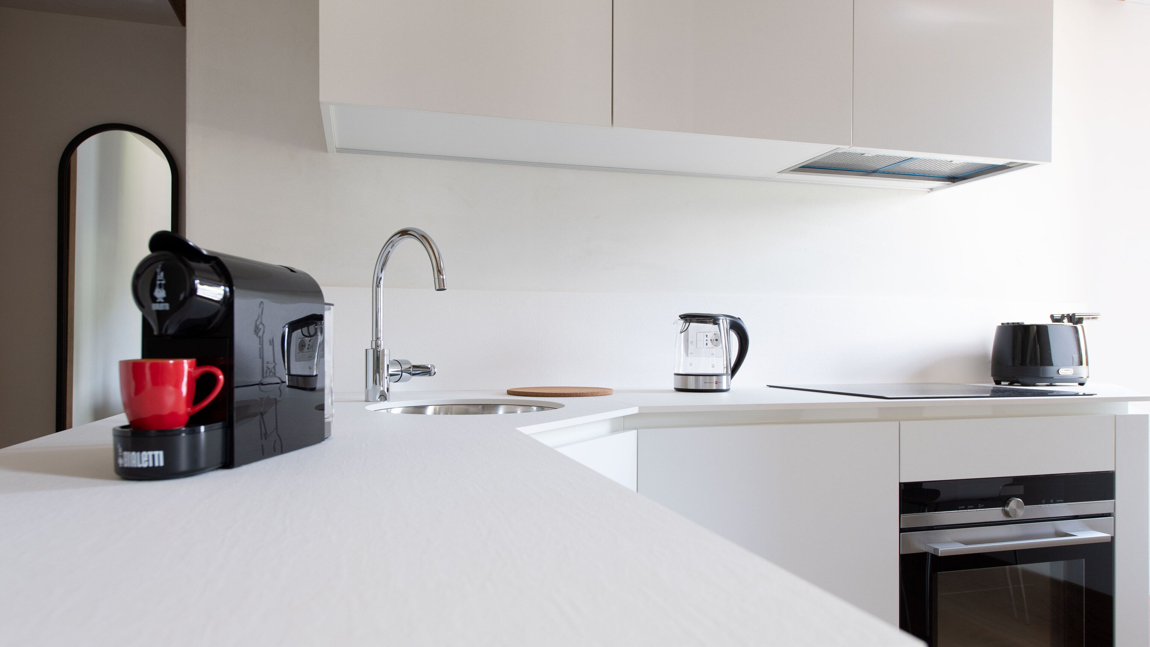 A modern kitchen with a coffee maker, a kettle, and a red cup on the counter.