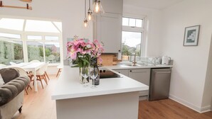 A modern kitchen with a large island, white cabinetry, and a view of the outdoors. - Shileen (Seahouses)
