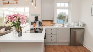 A modern kitchen with a central island, white cabinetry, a coffee machine, and a view of the outdoors. - Shileen (Seahouses)