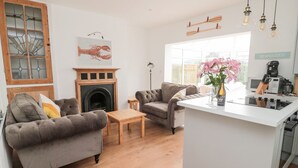 A modern living room with a fireplace, two sofas, a coffee table, and a kitchen area with a microwave and coffee maker. - Shileen (Seahouses)