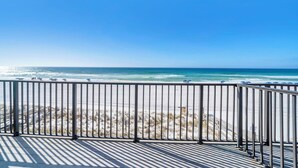 Une vue sur la plage depuis un balcon doté d’une balustrade, avec une plage de sable et l’océan en toile de fond.