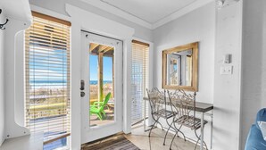 Une pièce avec vue sur la plage, une porte donnant sur l’extérieur, un coin repas avec des chaises et un canapé bleu.