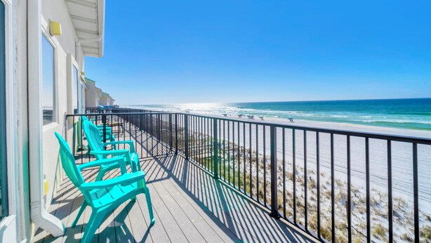 Un balcon avec des chaises turquoise donnant sur une plage, le tout bordé d’une rambarde en métal.