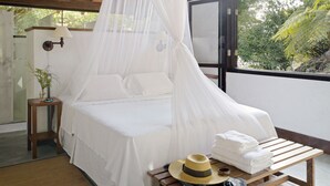 Una cama con dosel, una mesita de noche con lámpara y vista a zonas verdes al exterior.