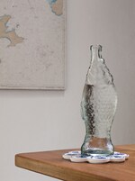A clear glass bottle with a textured surface, placed on a wooden surface with a coaster.
