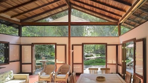 Amplia habitación con techo alto y ventanas grandes, que cuenta con un comedor de madera y vista al jardín.