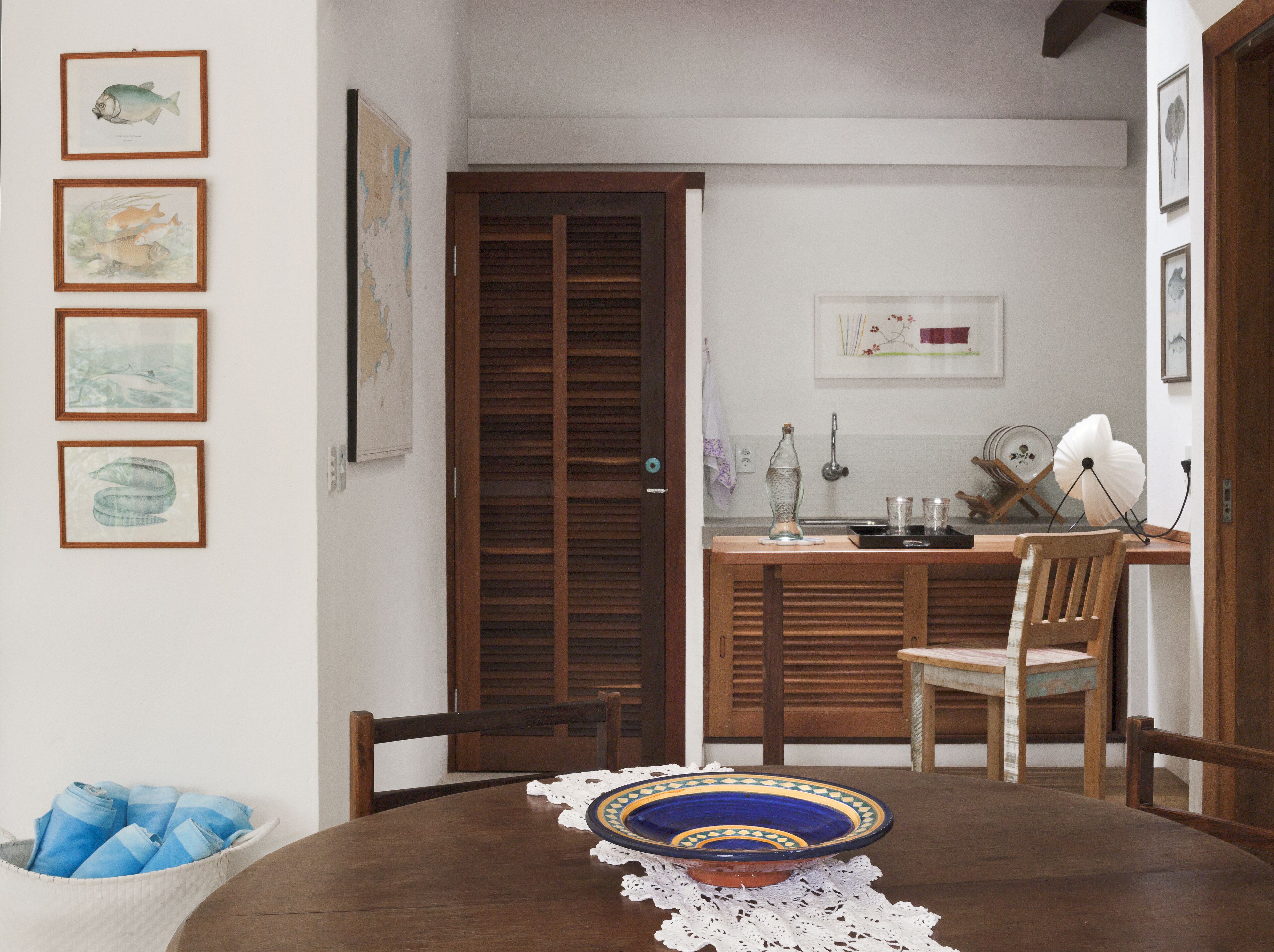A dining area with a round table, chairs, a decorative plate, and framed artwork on the wall.