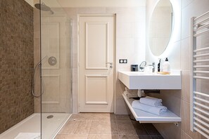 A modern bathroom with a glass-enclosed shower, a white door, a vanity with a mirror, and a towel rack. - L'Invitation au Voyage (Honfleur)