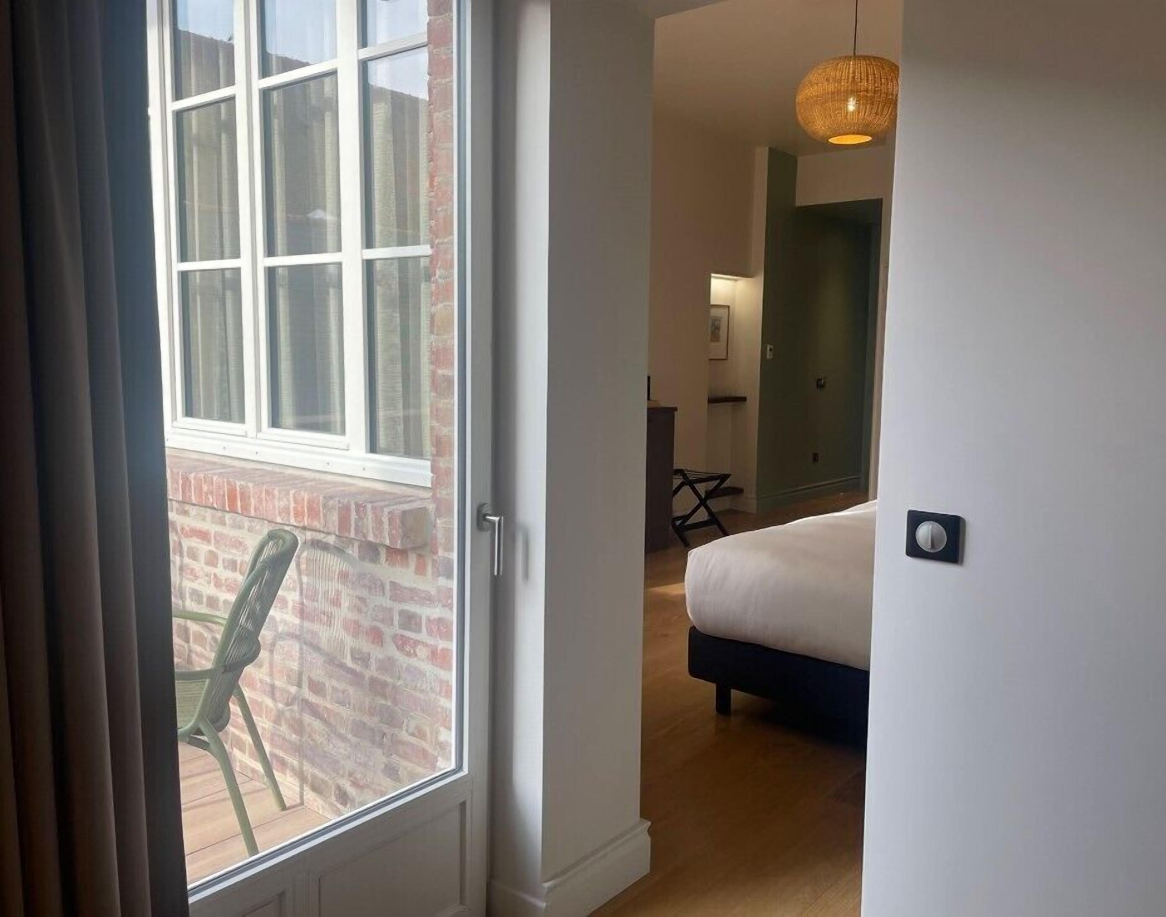 A hotel room with a large window, a bed, a desk, and a chair.