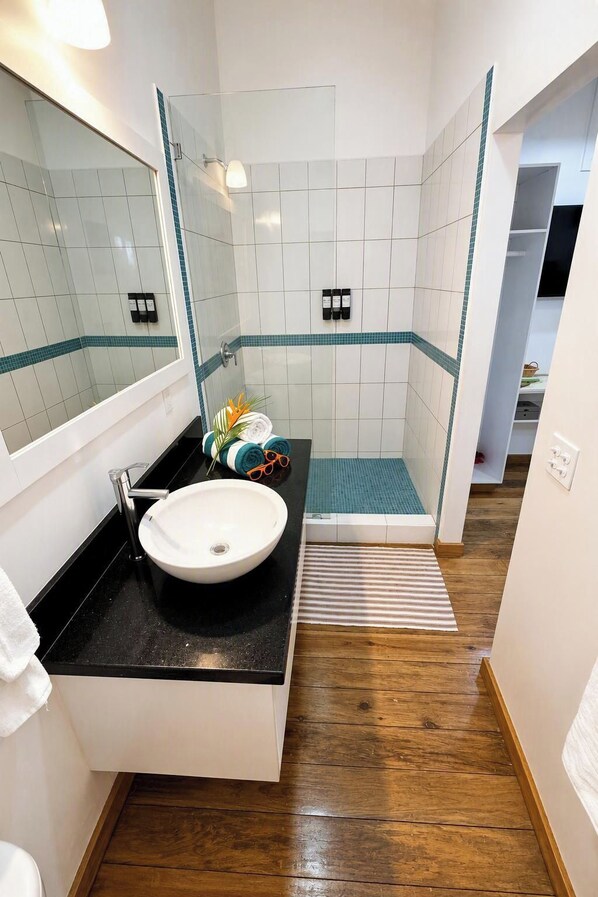 Et moderne badeværelse med en hvid vask, bordplade i sort og et brusekabine i glas.