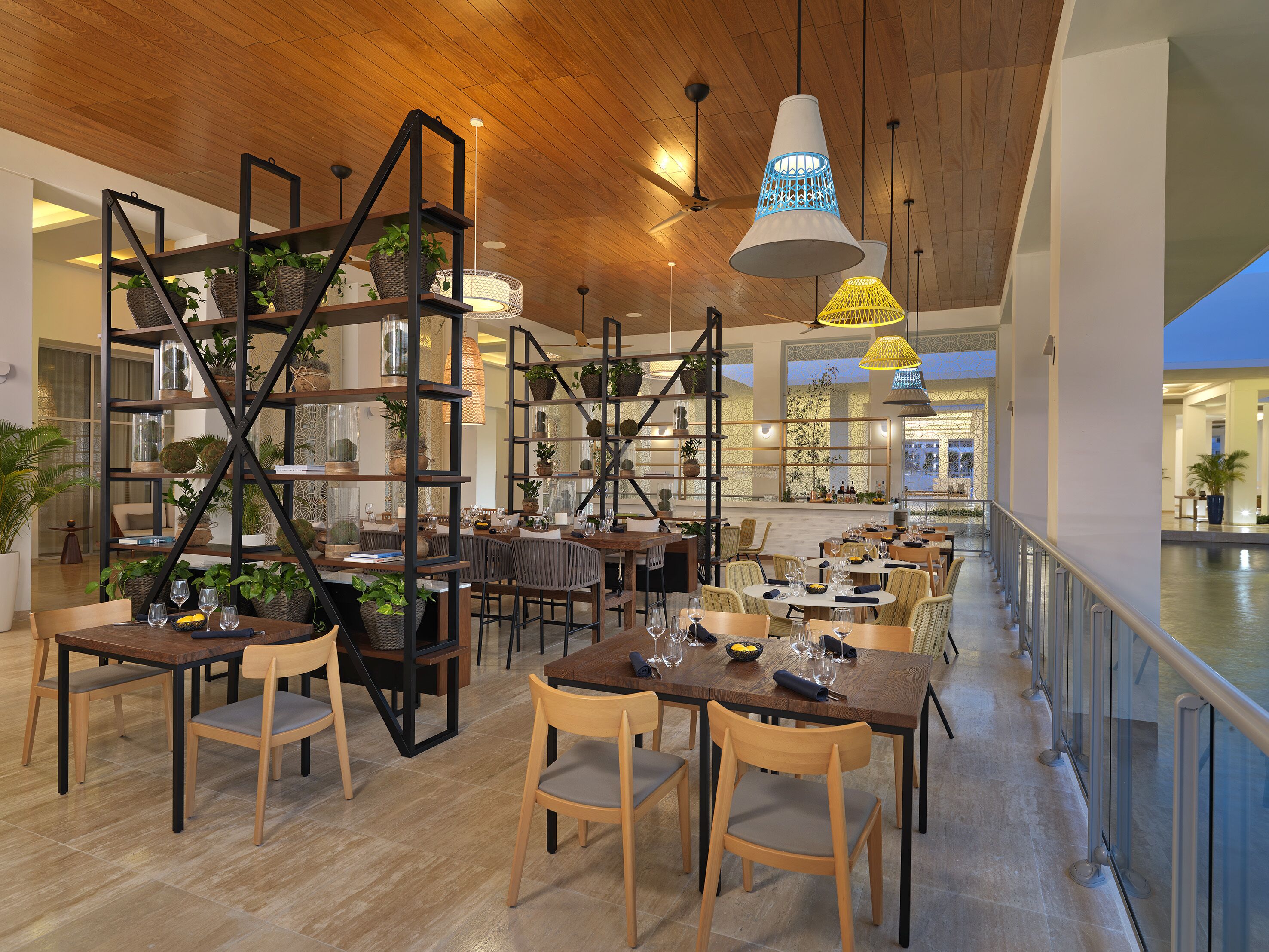 A spacious restaurant with high ceilings, wooden beams, and modern lighting fixtures. Tables are arranged for dining, and there are multiple seating areas.