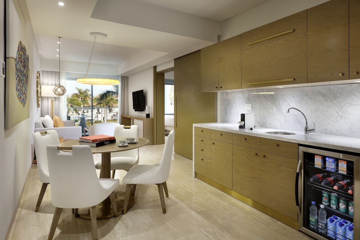 A modern kitchen with wooden cabinets, a built-in refrigerator, and a dining area with white chairs and a round table.