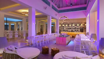 A spacious indoor area with a long dining table, several chairs, and a bar area.