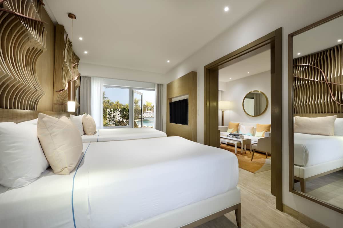 A modern hotel room with a large bed, a sitting area with a TV, and a view of the outdoors.