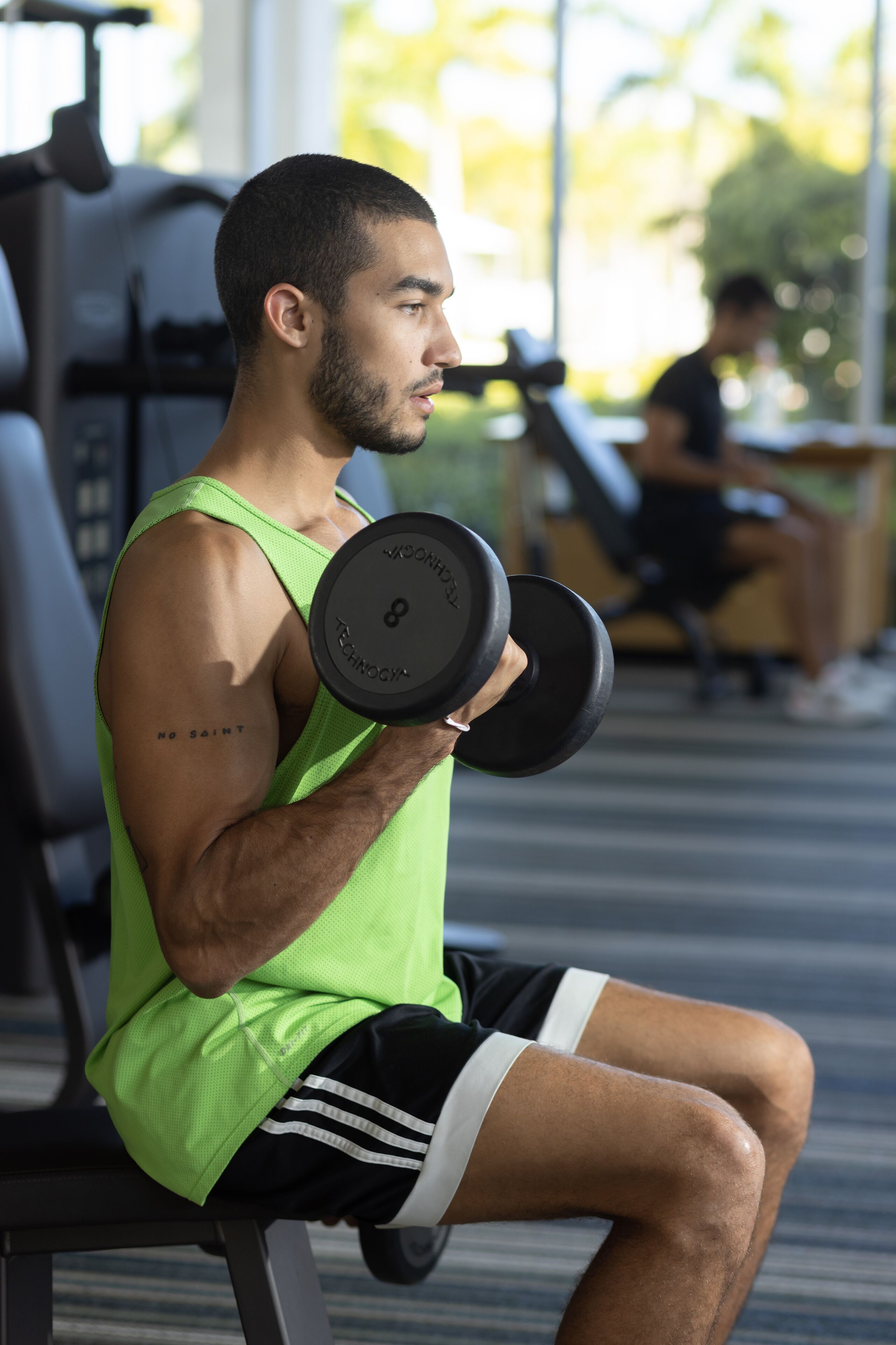 A person sitting on a bench in a gym, holding a dumbbell.