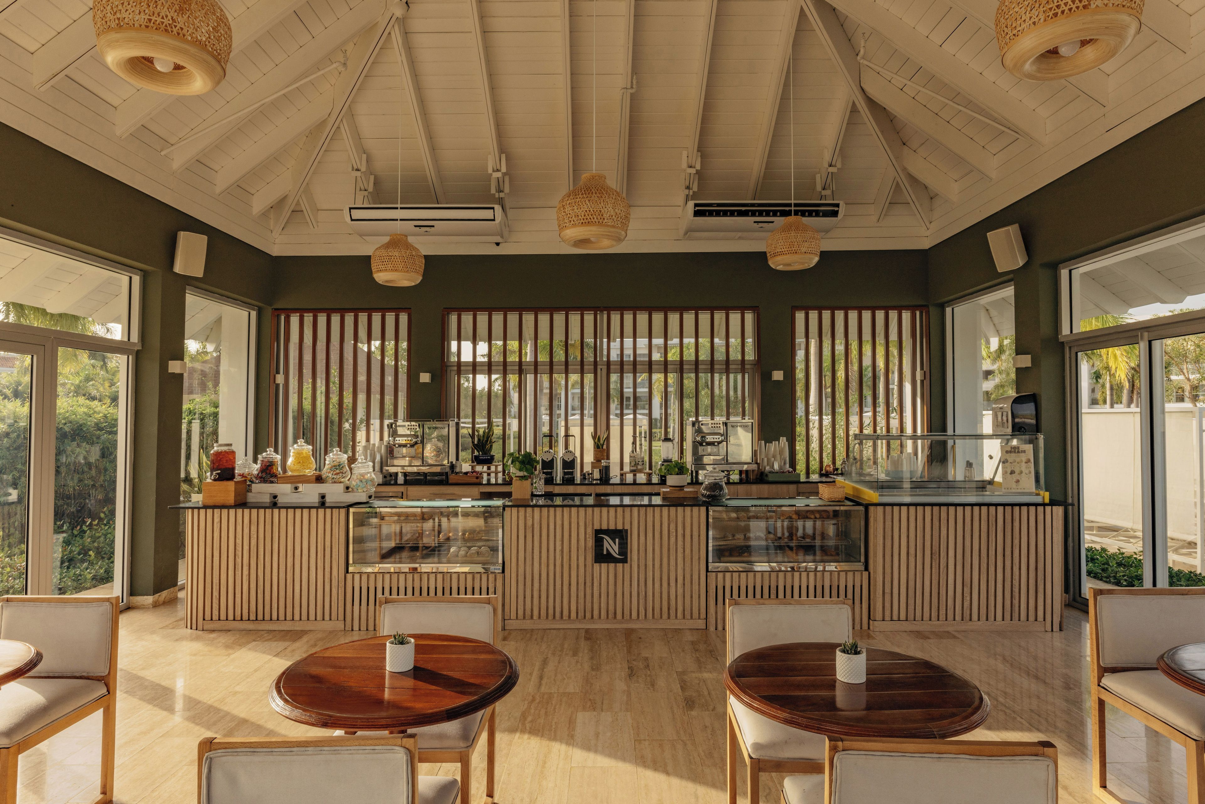 Un café doté d’un comptoir en bois, d’une vitrine réfrigérée et d’un espace salon avec des tables et des chaises rondes.
