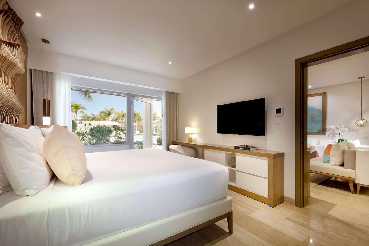 A modern hotel room with a large bed, a TV, a desk, and a view of palm trees.