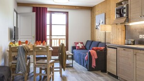 Ett mysigt vardagsrum med ett matbord och stolar i trä, en soffa och ett kök med träskåp och en mikrovågsugn.