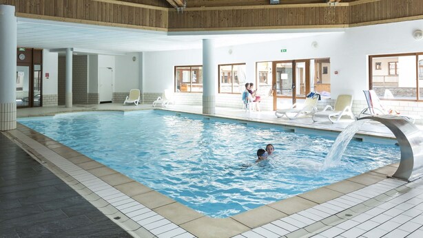 En inomhuspool med klart vatten, omgiven av solstolar och ett tak av trä.