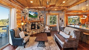 A rustic cabin interior with a stone fireplace, wooden ceiling, and a cozy seating area. - Designer Chalet | Sauna · Fireplace · Mountain Views (Big Bear Lake)