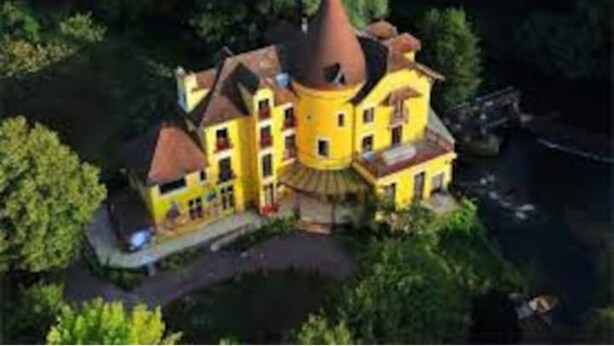 Un grand bâtiment jaune, doté d’une tour remarquable, et entouré de verdure.