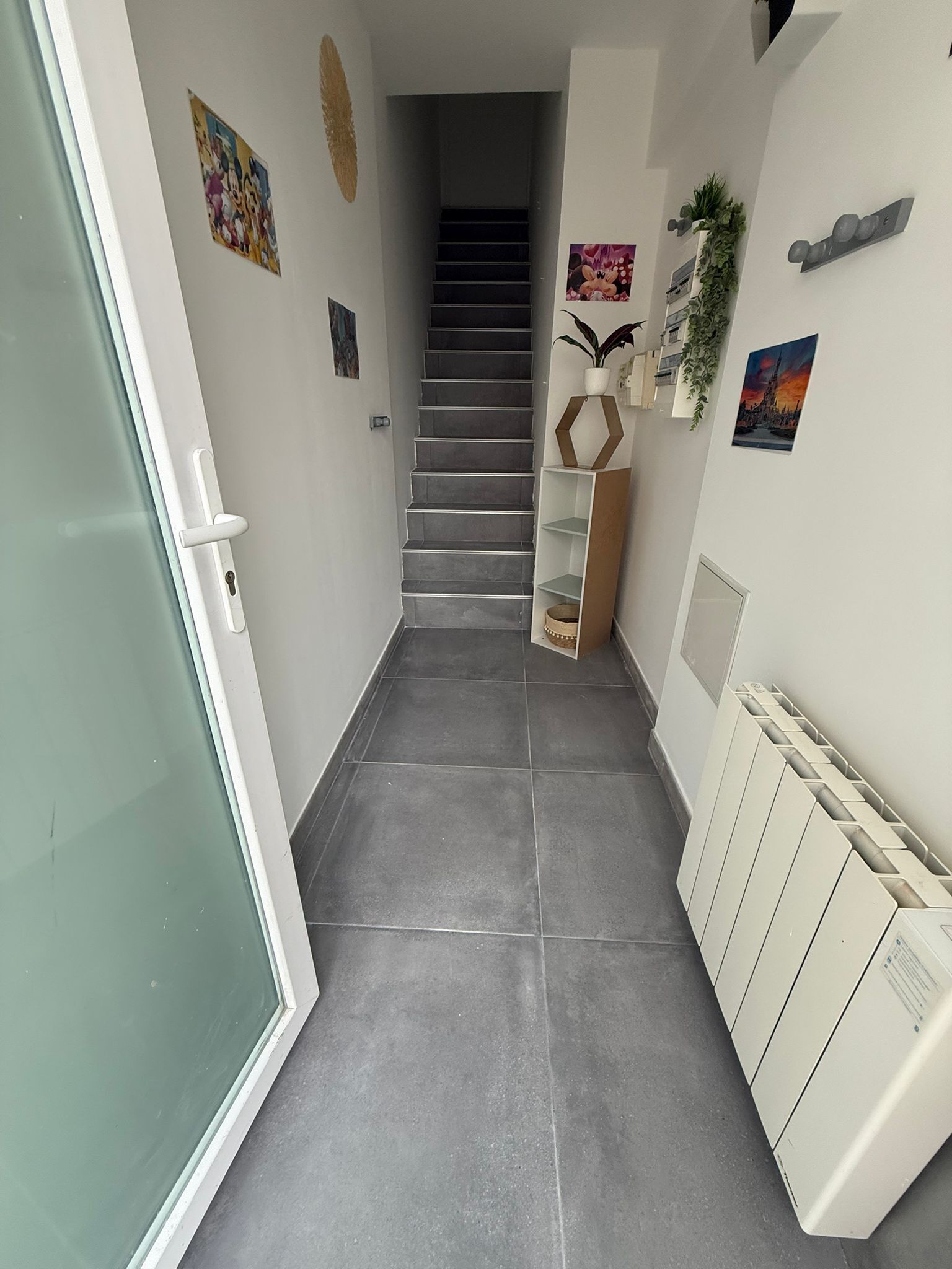 Ein Flur mit grauen Fliesen, einer Treppe und einem Heizkörper rechts.