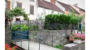 Un quartier résidentiel doté d’un escalier en pierre menant à une entrée fermée par un portail, le tout entouré de verdure et de plantes à fleurs.