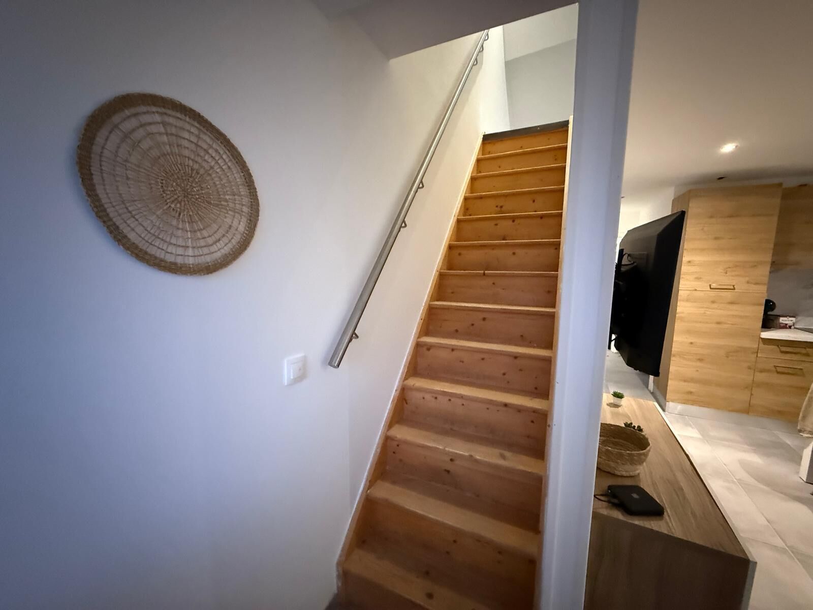 Eine Holztreppe führt zu einer zweiten Etage, eine gewebte Wanddecke und ein moderner Küchenbereich mit Holzschränken und einer Arbeitsplatte.