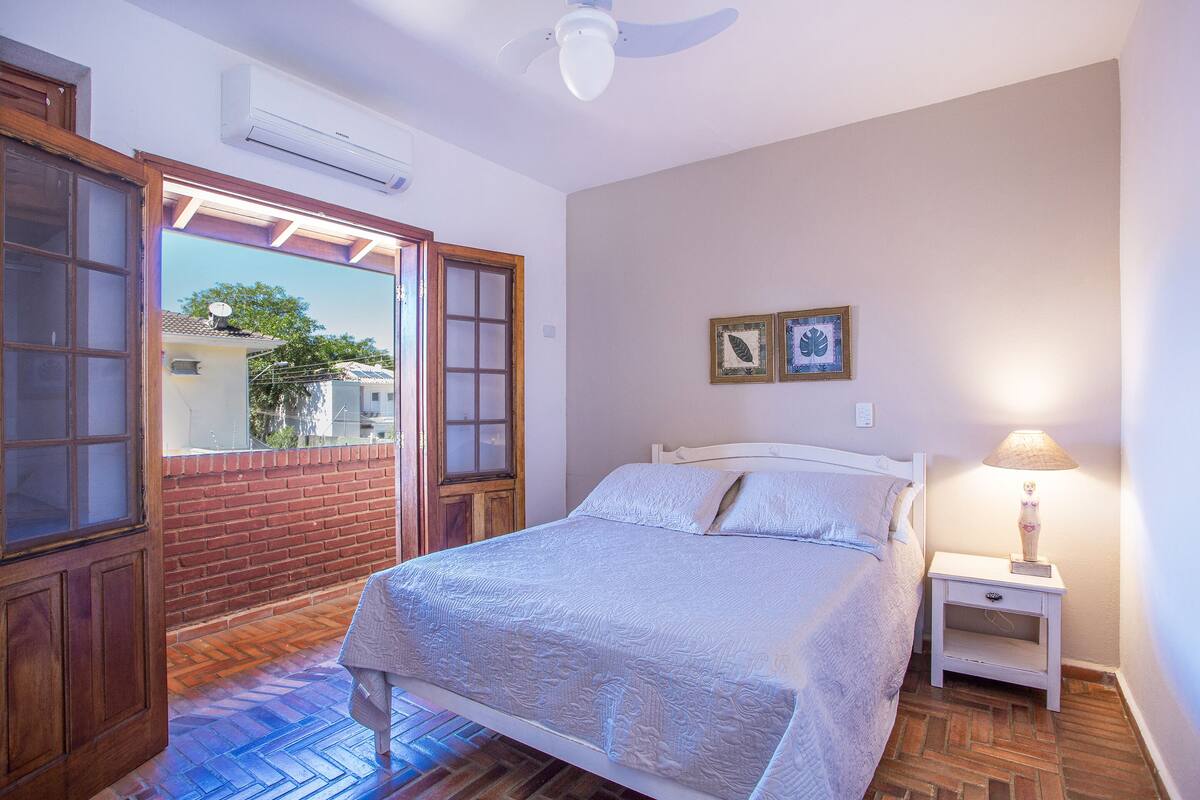 A bedroom with a bed, a nightstand, a lamp, a ceiling fan, and a view through a door.