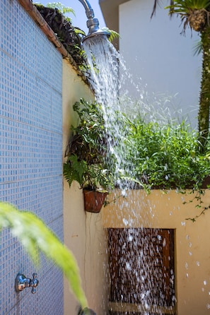 A shower with water flowing over a tiled wall and plants. - Residencial Santa Lucia (São Sebastião)