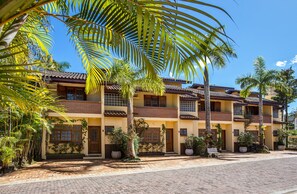 A multi-story building with a tiled roof, surrounded by palm trees and potted plants. - Residencial Santa Lucia (São Sebastião)